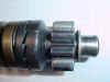 From right to left; the end of the shaft that protrudes into the bearing that is in the rear cover, the washer, the small spring that is barely visible, the kick start gear with its ratchet teeth, the matching teeth and on the far left is the cushion spring. The ratcheting teeth are shown just as they are about to snap over each other. 
